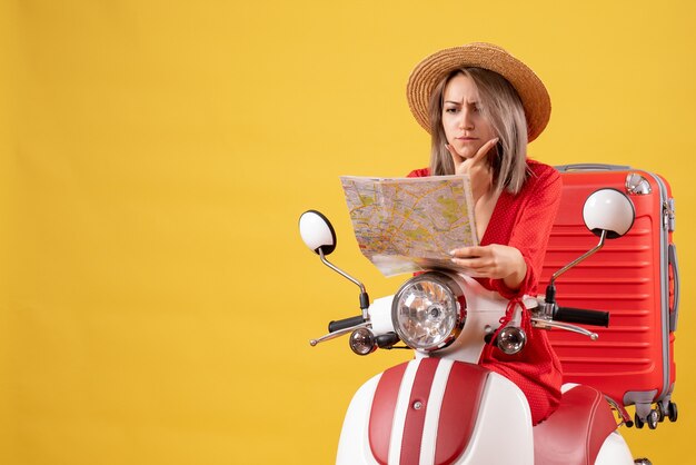 Chica guapa en ciclomotor con maleta roja mirando el mapa