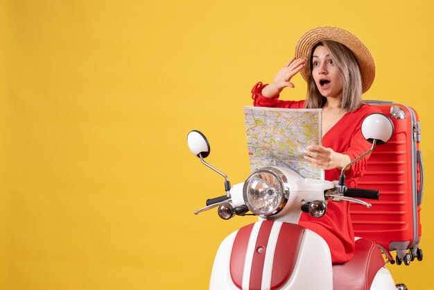 Chica guapa en ciclomotor con maleta roja sosteniendo un mapa llamando a alguien