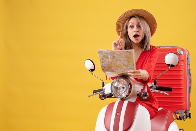 Chica guapa en ciclomotor con maleta roja sosteniendo un mapa sorprendente con una idea