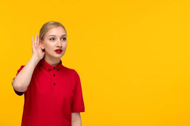 Chica guapa del día de la camisa roja escuchando a escondidas en una camisa roja sobre un fondo amarillo