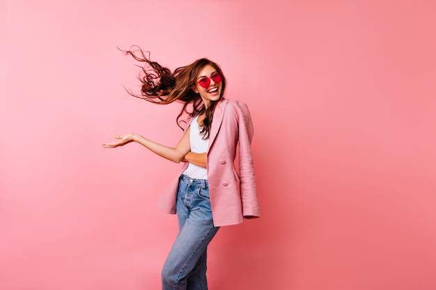 Chica guapa emocionada en gafas de sol bailando. Mujer dichosa de jengibre posando en rosa con cabello ondulado.