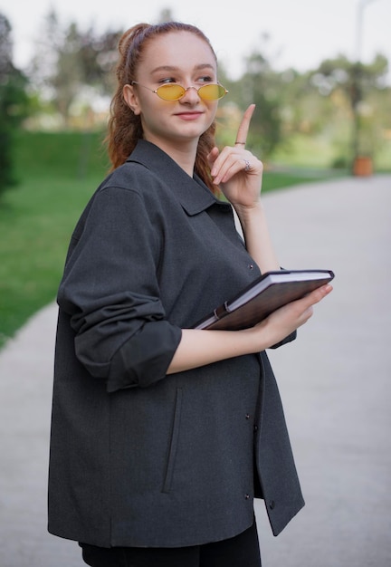 Chica guapa con gafas de sol de pie apuntando hacia arriba con el dedo