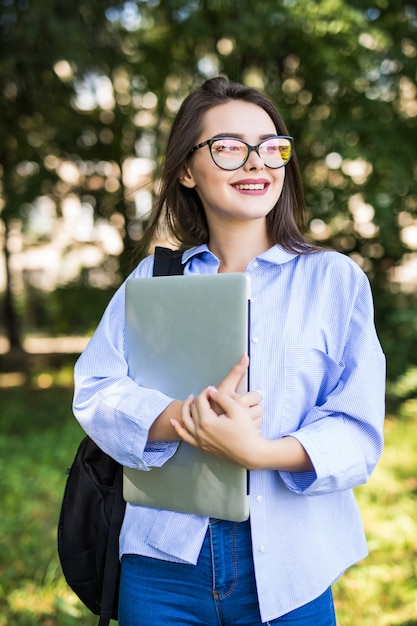 Chica guapa con gafas transparentes se queda con su computadora portátil en el parque