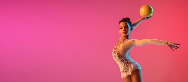 Chica guapa gimnasta rítmica afroamericana practicando en pared degradada en luz de neón