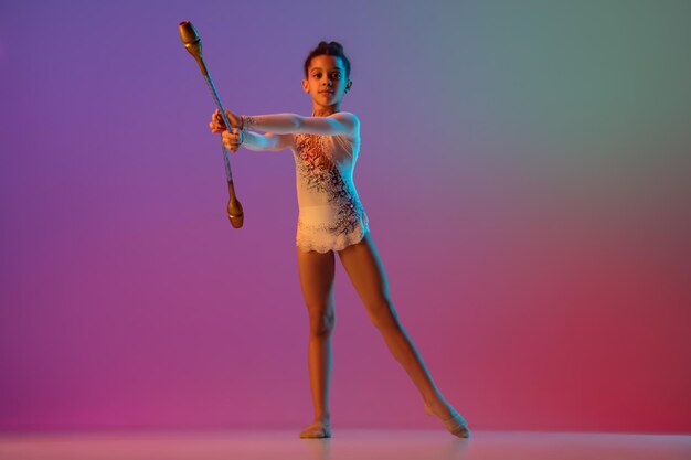 Chica guapa gimnasta rítmica afroamericana practicando sobre fondo de estudio degradado con luz de neón