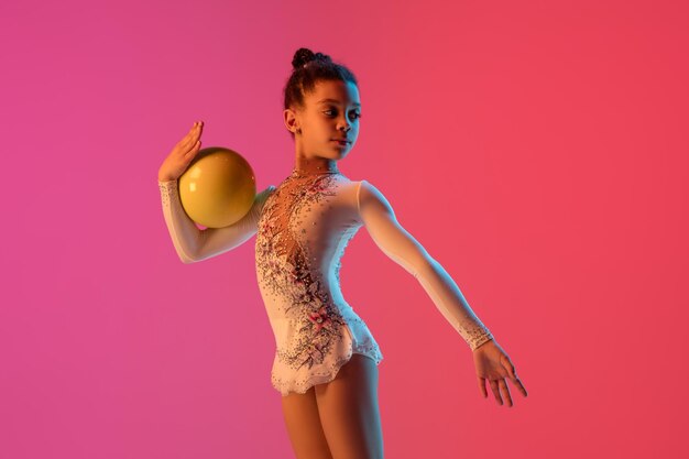 Chica guapa gimnasta rítmica afroamericana practicando sobre fondo de estudio degradado con luz de neón