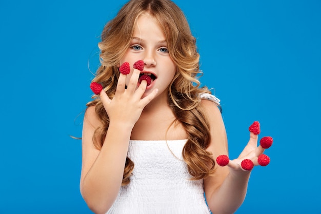 Foto gratuita chica guapa joven comiendo frambuesa sobre pared azul