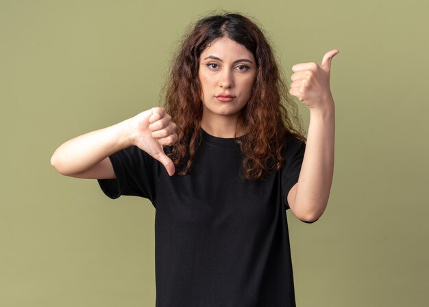 Chica guapa joven disgustada mostrando los pulgares hacia arriba y hacia abajo aislado en la pared verde oliva