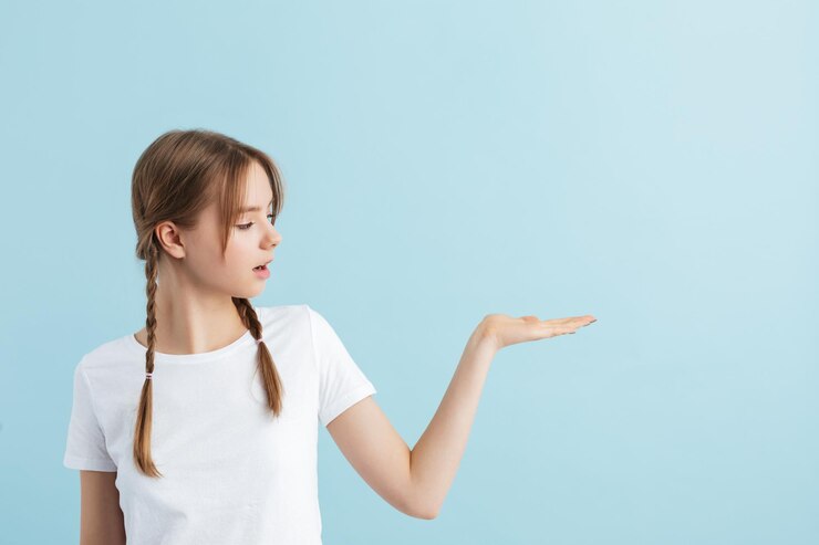 Foto gratuito chica guapa joven con dos trenzas en camiseta blanca mirando soñadoramente a un lado mostrando copyspace invisible sobre fondo azul aislado