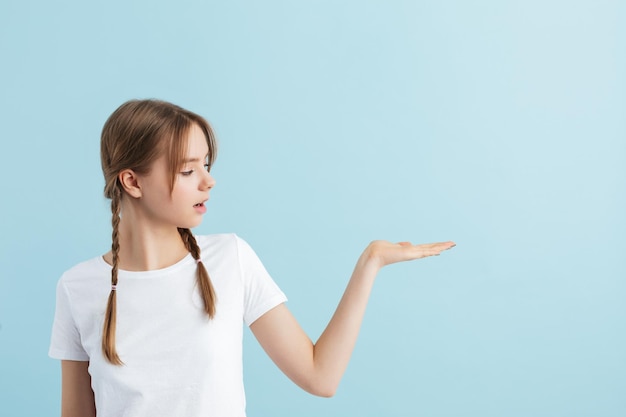 Chica guapa joven con dos trenzas en camiseta blanca mirando soñadoramente a un lado mostrando copyspace invisible sobre fondo azul aislado