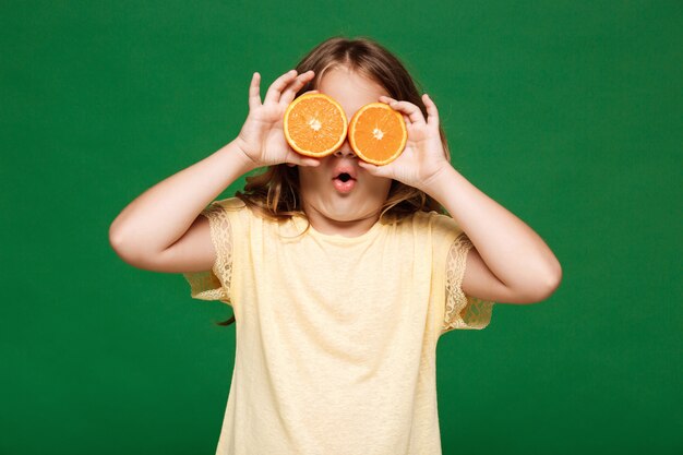 Chica guapa joven escondiendo los ojos con naranjas sobre pared verde