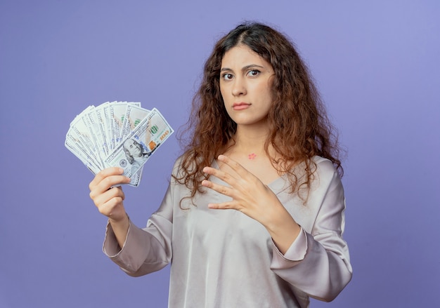 Foto gratuita chica guapa joven estricta sosteniendo dinero en efectivo y mostrando cuatro aislados en la pared azul