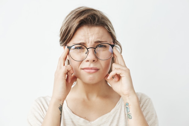 Chica guapa joven en gafas pensando frunciendo el ceño con los dedos en las sienes.