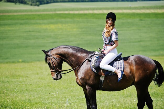 Chica guapa joven montando un caballo en un campo en un día soleado