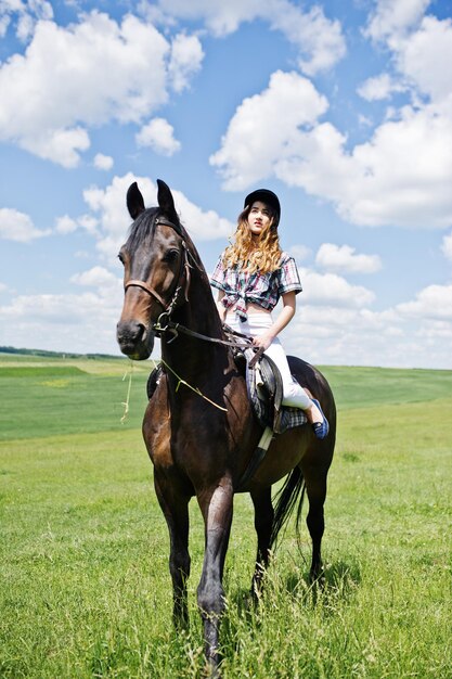 Chica guapa joven montando un caballo en un campo en un día soleado