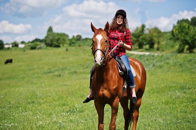 Chica guapa joven montando un caballo en un campo en un día soleado