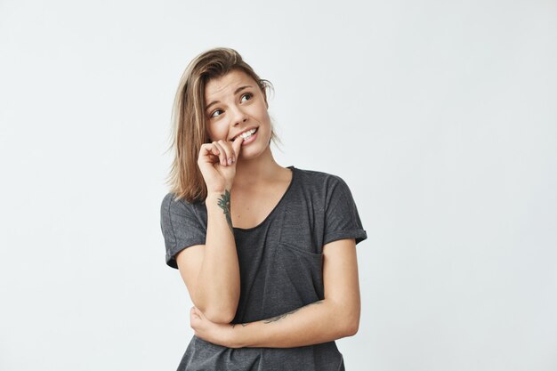 Chica guapa joven nerviosa mirando en las uñas mordidas.