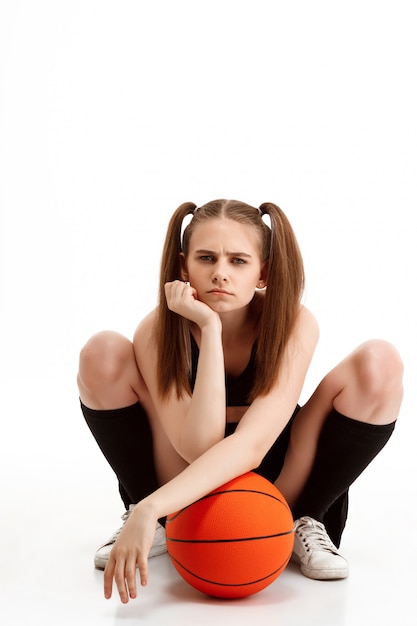 Chica guapa joven posando con baloncesto sobre pared blanca