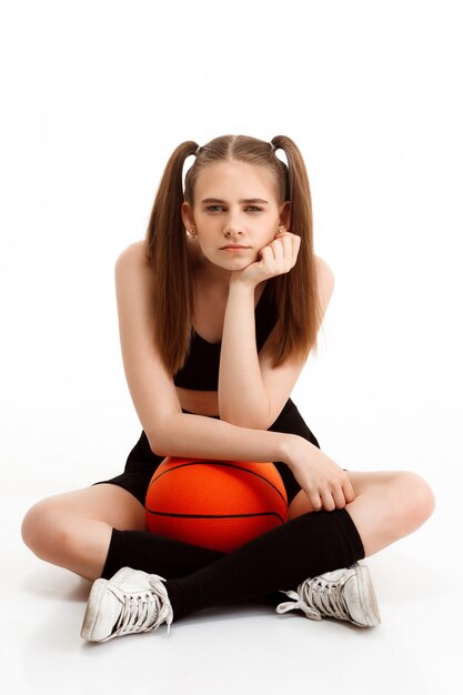 Chica guapa joven posando con baloncesto sobre pared blanca