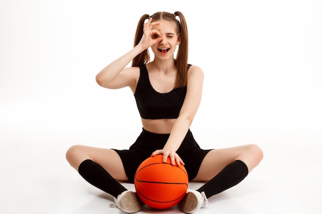 Foto gratuita chica guapa joven posando con baloncesto sobre pared blanca