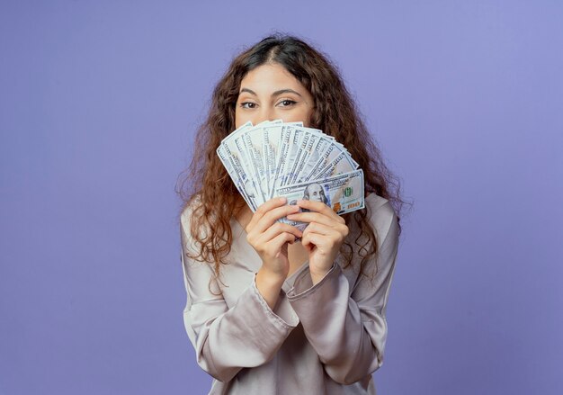 Chica guapa joven rostro cubierto con dinero aislado en la pared azul