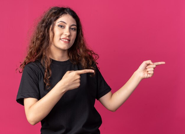 Chica guapa joven sonriente apuntando al lado