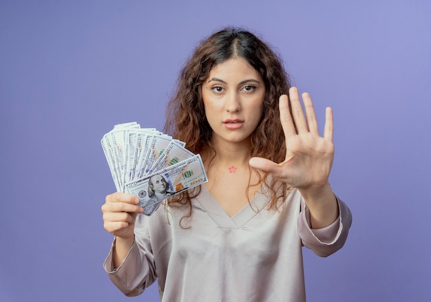 Foto gratuita chica guapa joven sosteniendo dinero en efectivo y mostrando gesto de parada