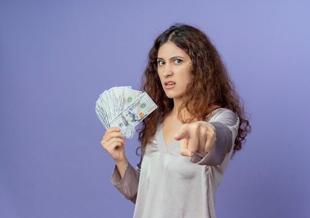 Chica guapa joven sosteniendo dinero y mostrándole gesto aislado en la pared azul