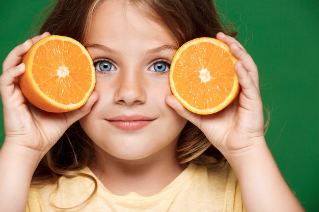 Chica guapa joven sosteniendo naranja sobre pared verde