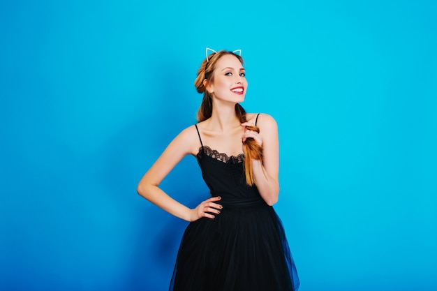 Chica guapa joven vestida para la fiesta, sonriendo y posando. Con un elegante vestido negro y una diadema de orejas de gato con diamantes, un bonito maquillaje, manicura dorada.