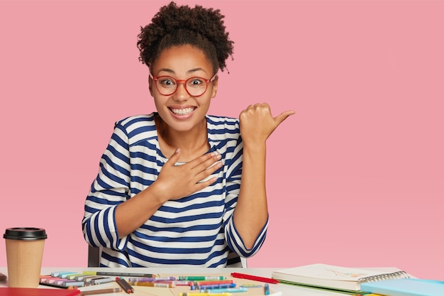 Una chica guapa de piel oscura se ve alegre, no puedo creer en cosas positivas, crea un proyecto creativo