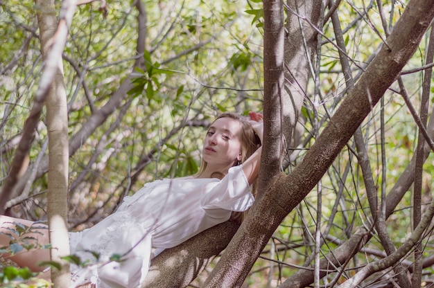 Chica guapa posando tumbada en un árbol