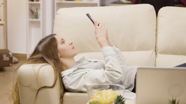 Chica guapa relajante en el sofá con su teléfono inteligente. Novio en el fondo.