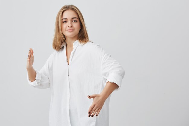 Chica guapa rubia con camisa blanca moviéndose como un robot, mirando. Hermosa chica caucásica con pelo rubio divirtiéndose.