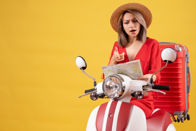 Chica guapa con sombrero de Panamá en ciclomotor con maleta roja mirando el mapa