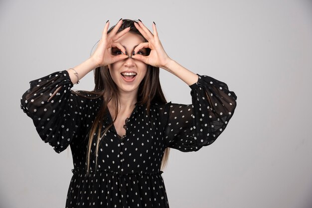 Chica guapa con sonrisa sosteniendo los dedos cerca de los ojos como gafas.