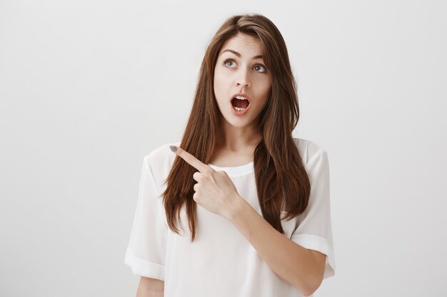 Chica guapa sorprendida e impresionada mirando y señalando la esquina superior izquierda