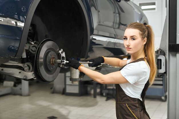 Chica guapa trabajando como mecánico en autoservicio, reparación de automóviles.