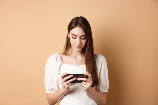 Chica guapa viendo videos en el teléfono inteligente sosteniendo el teléfono móvil horizontalmente y mirando la pantalla ...