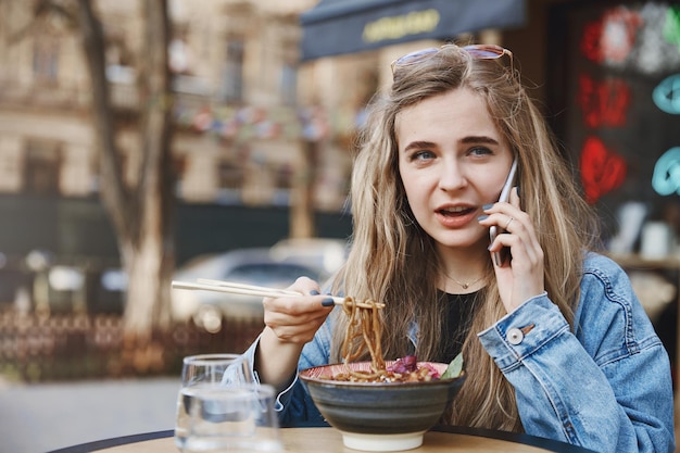 Chica guiando a un amigo a través de un teléfono inteligente comiendo en un restaurante asiático