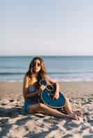 Foto gratuita chica con guitarra sentada en la playa