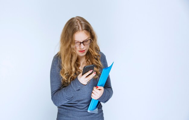 Chica hablando por teléfono de forma insatisfecha y haciendo correcciones en su carpeta azul.