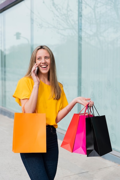 Chica hablando por teléfono mientras sostiene bolsas de compras