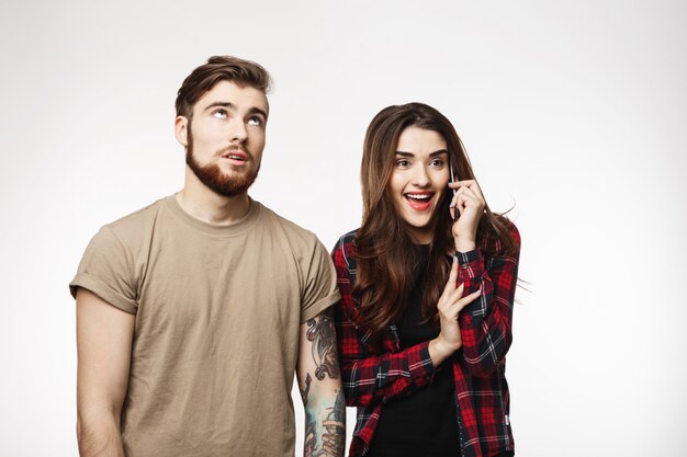 Chica hablando por teléfono sonriendo felizmente, novio agotado mirando a otro lado.