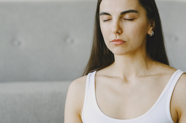 Foto gratuita chica haciendo ejercicios de yoga en casa cerca de un sofá y una ventana en ropa deportiva