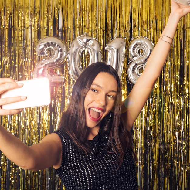 Chica haciendo un selfie con smartphone brilloso en celebración de año nuevo