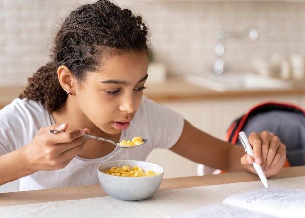 Chica haciendo sus deberes mientras desayuna