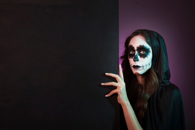 Chica de halloween con makeup detrás de pared