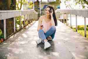 Foto gratuita chica hermosa y brillante en camisetas rosas y jeans sentados en el parque de verano soleado