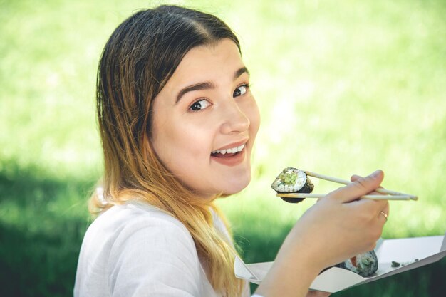 Una chica hermosa come sushi sentada en el césped del parque